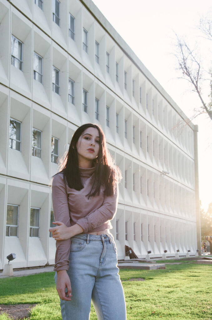 Gabriela Inzunza stands in front of a modern building with a unique geometric design bathed in the soft glow of the setting sun.